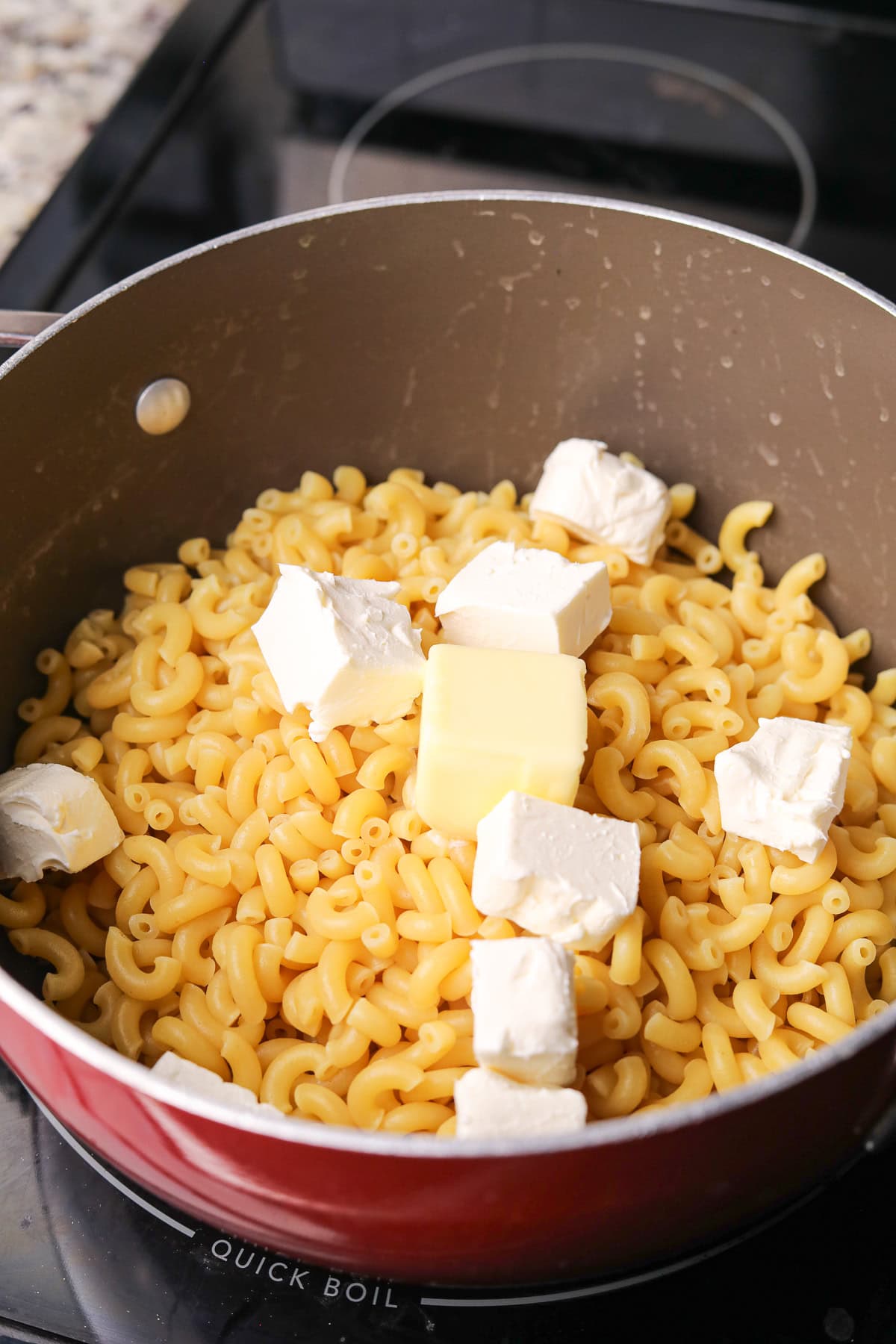 Cooked elbow macaroni in a pot with butter and cream cheese.