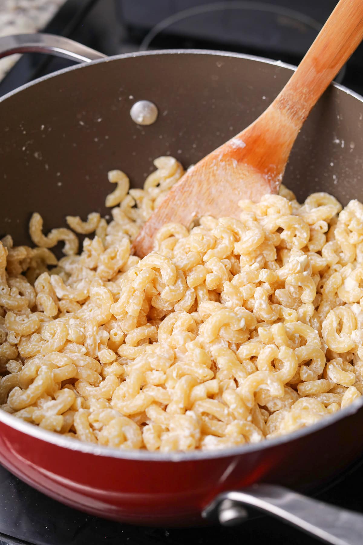 Cooked elbow macaroni combined with butter and cream cheese in a pot.