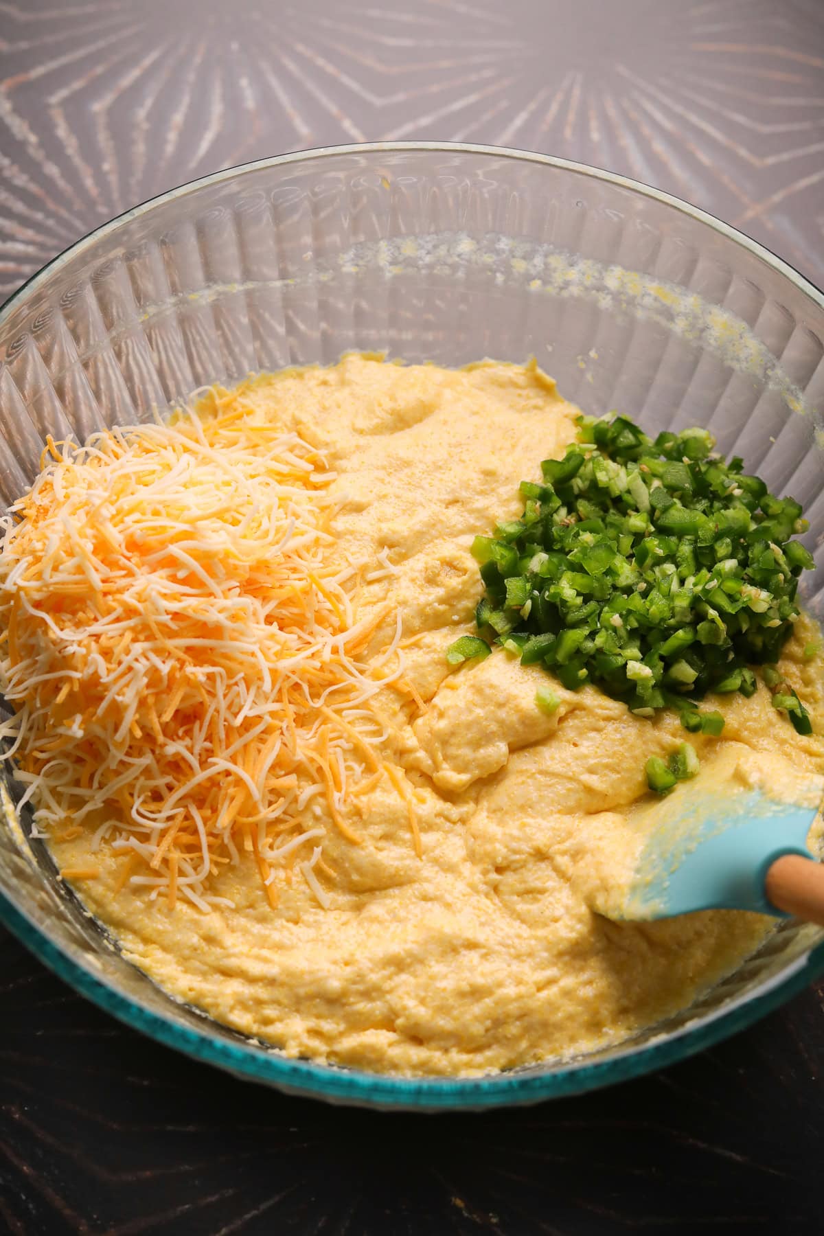Jalapeño cheddar cornbread batter with cheddar cheese and diced jalapeños in a mixing bowl.