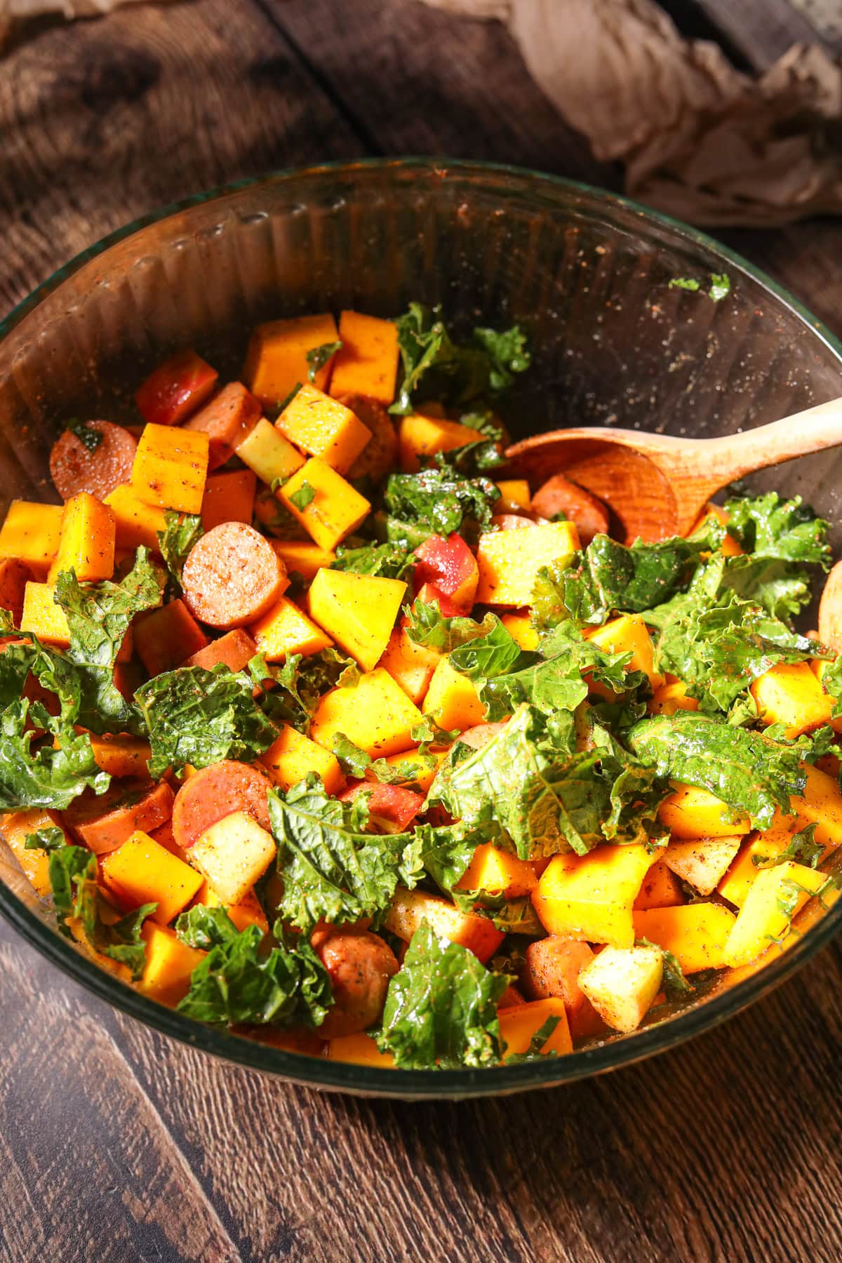 Ingredients for making chicken, apple sausage and butternut squash sheet pan meal being tossed in a large mixing bowl.
