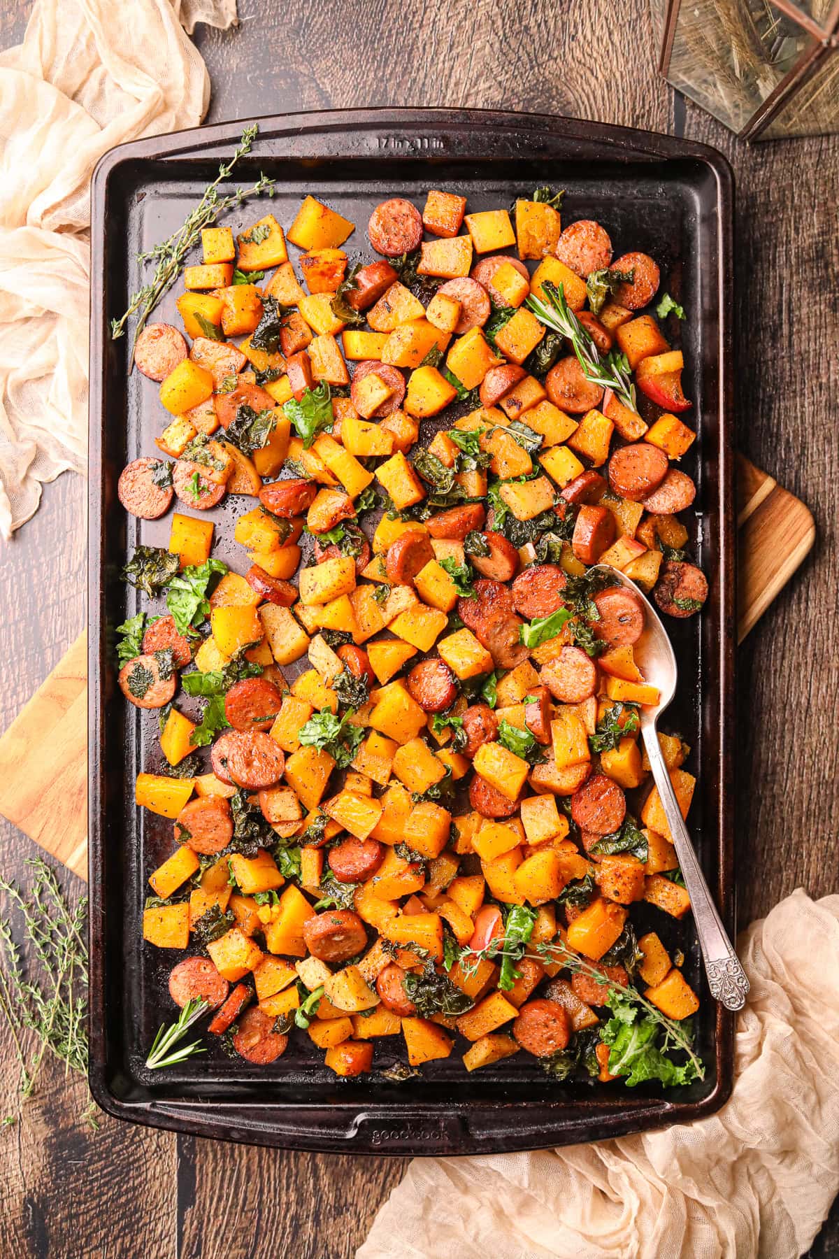Chicken sausage and butternut squash, sheet pan meal sitting on a table top with a serving spoon in the sheet pan.