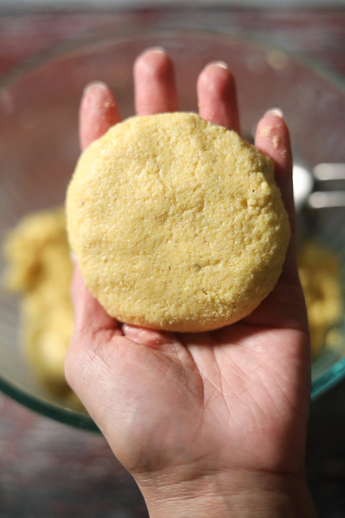 Uncooked hot water cornbread patty held in hand.
