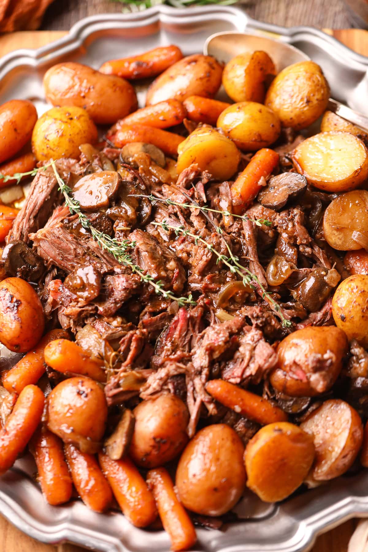  Shredded Dutch oven pot roast on a platter with veggies and herbs.