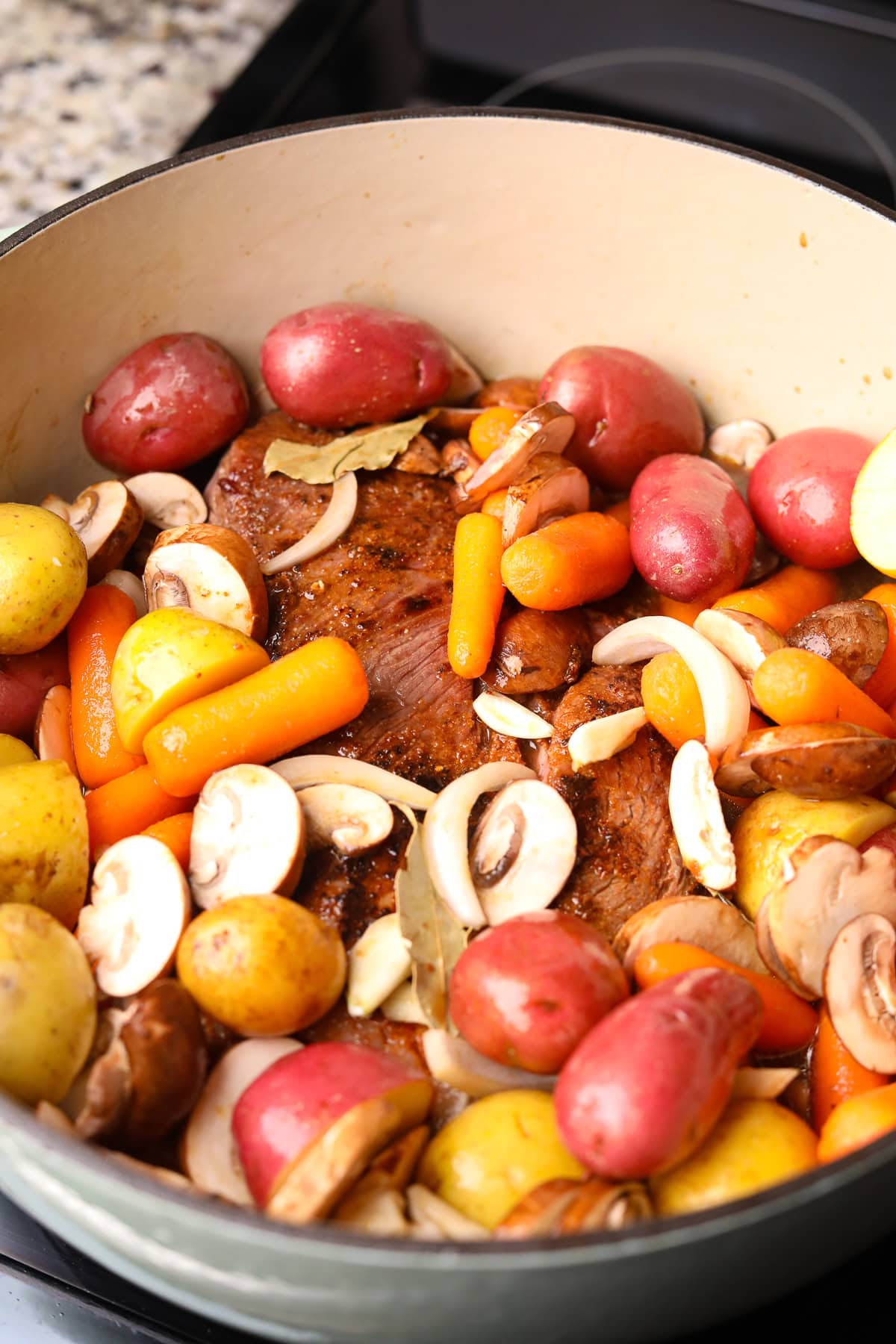  Chuck roast with vegetables in a Dutch oven before being baked.