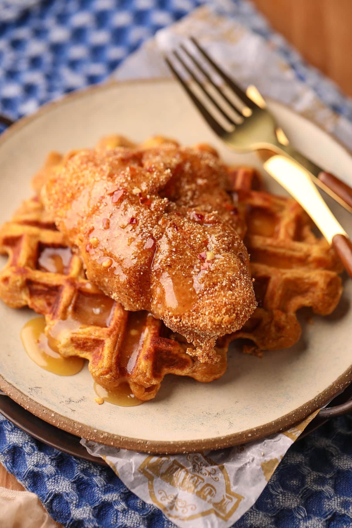 Sweet potato waffles, with fried catfish and spicy honey butter on a gray plate on a table top.