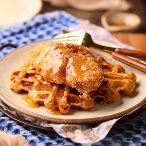 Sweet potato waffles, with fried catfish and spicy honey butter on a gray plate on a table top.