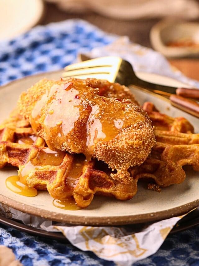 Sweet potato waffles, with fried catfish and spicy honey butter on a gray plate on a table top.