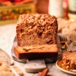 Apple butter, banana bread with pecan streusel on a serving board sitting on a table top.