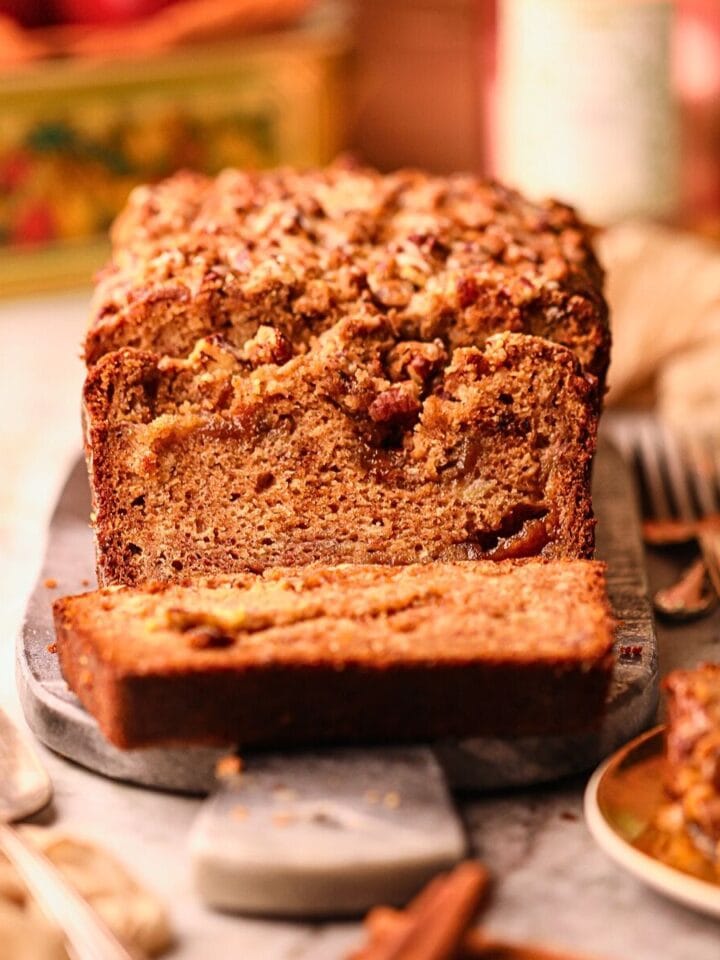 Apple butter, banana bread with pecan streusel on a serving board sitting on a table top.