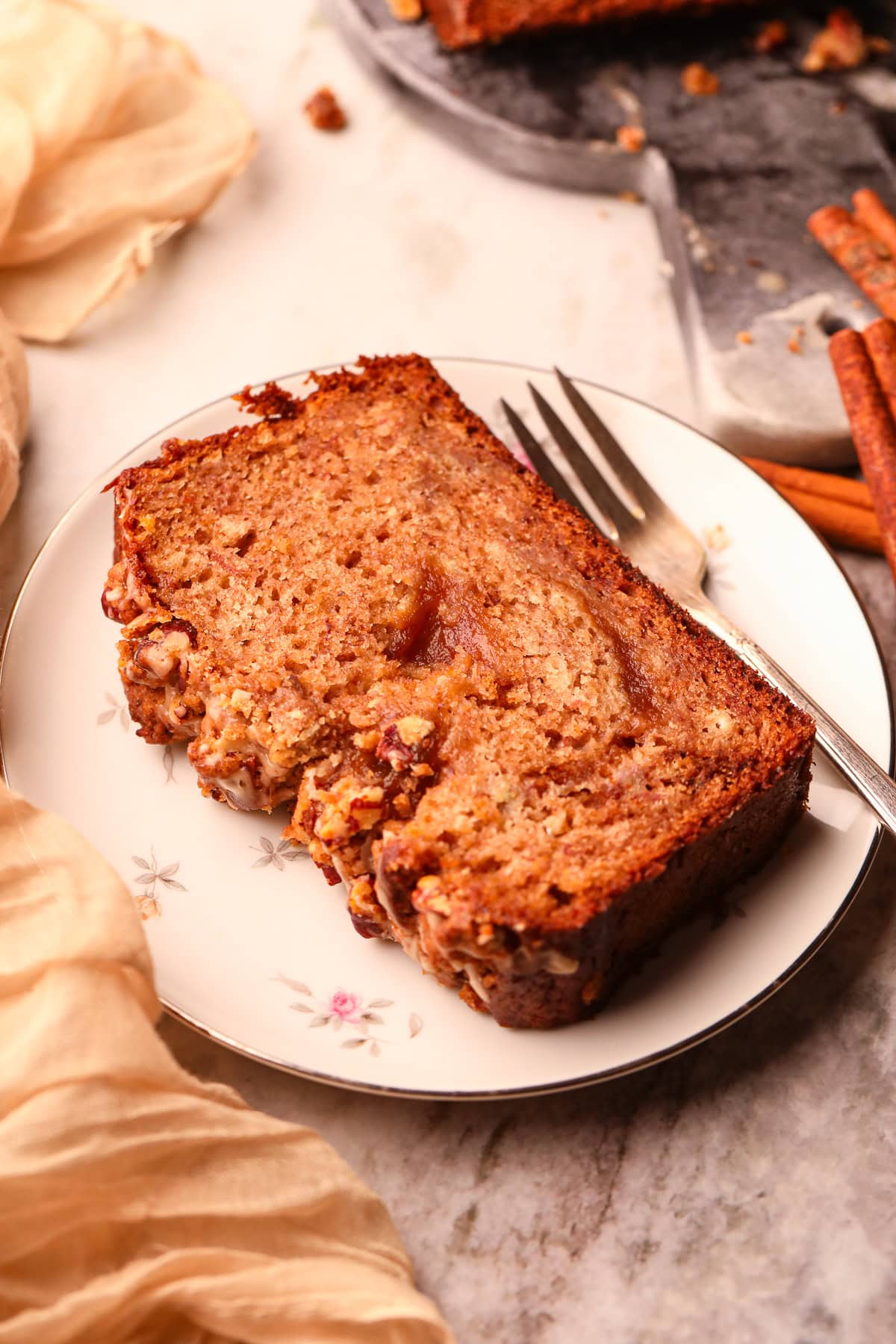 A slice of apple butter, banana bread with pecan streusel on a white dessert plate with a fork.