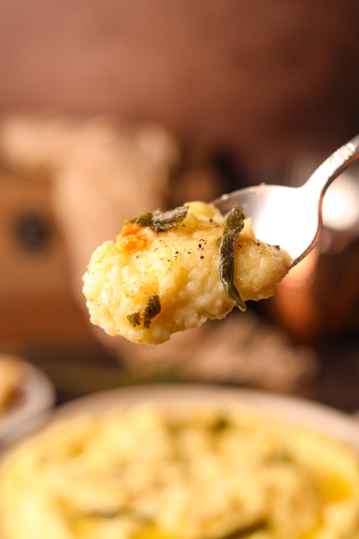 Brown butter, sage, mashed potatoes on a serving spoon to show texture.