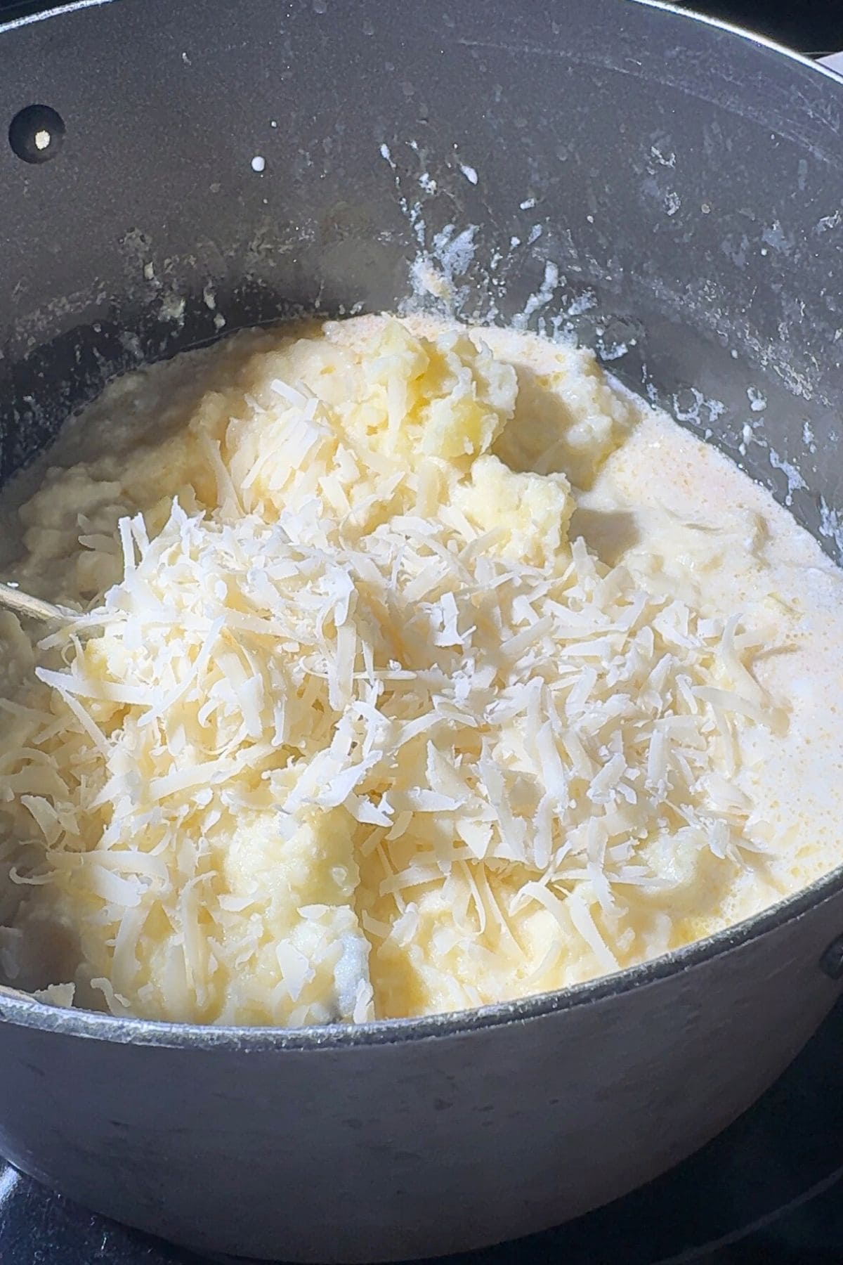 Mashed potatoes in a pot with cream and Parmesan cheese.