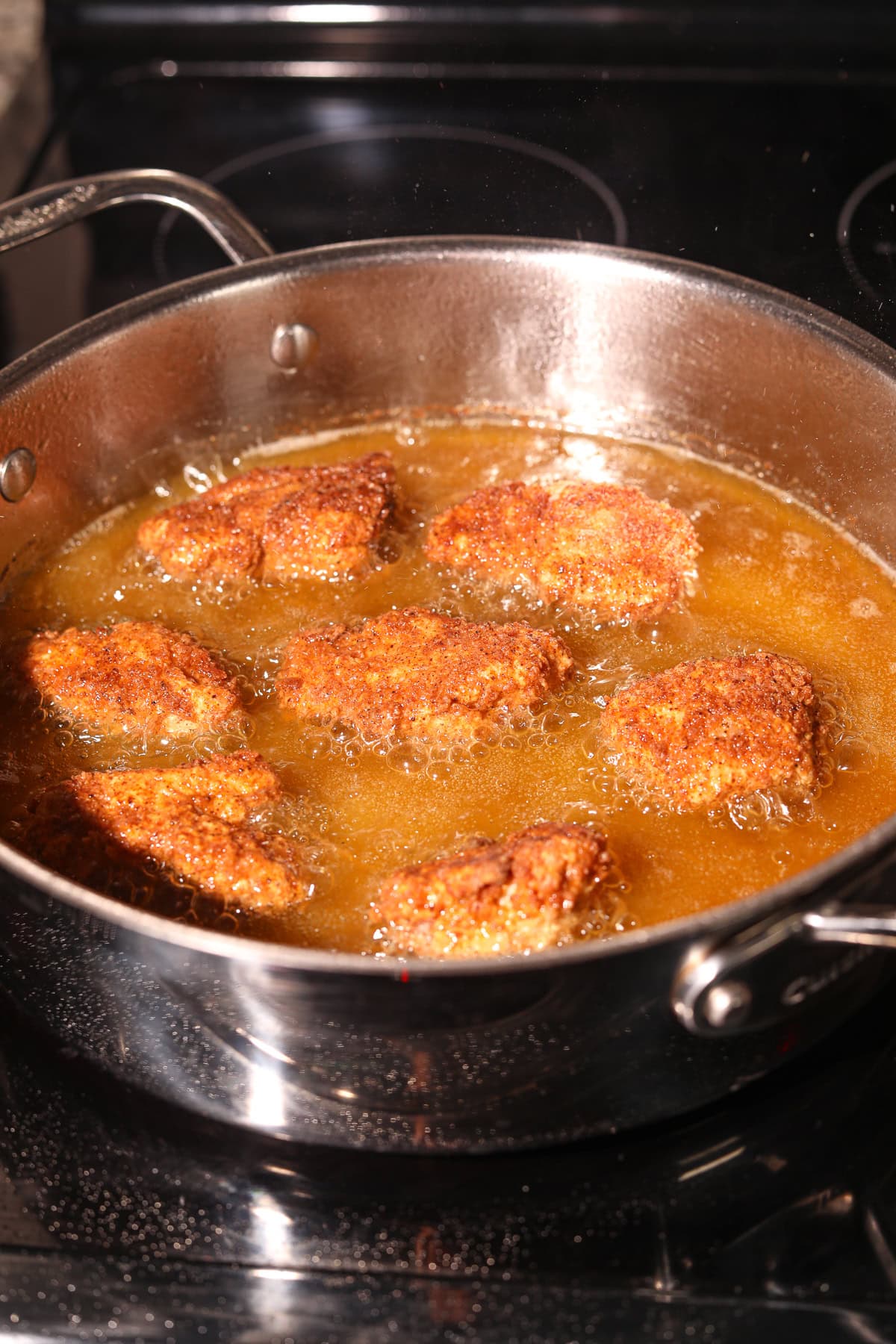 Breaded chicken chunks frying in a pan.