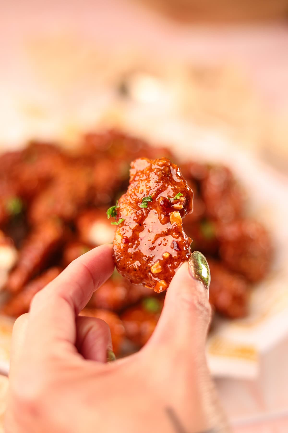 Crispy hot honey, garlic chicken bite, held in hand to show detail.