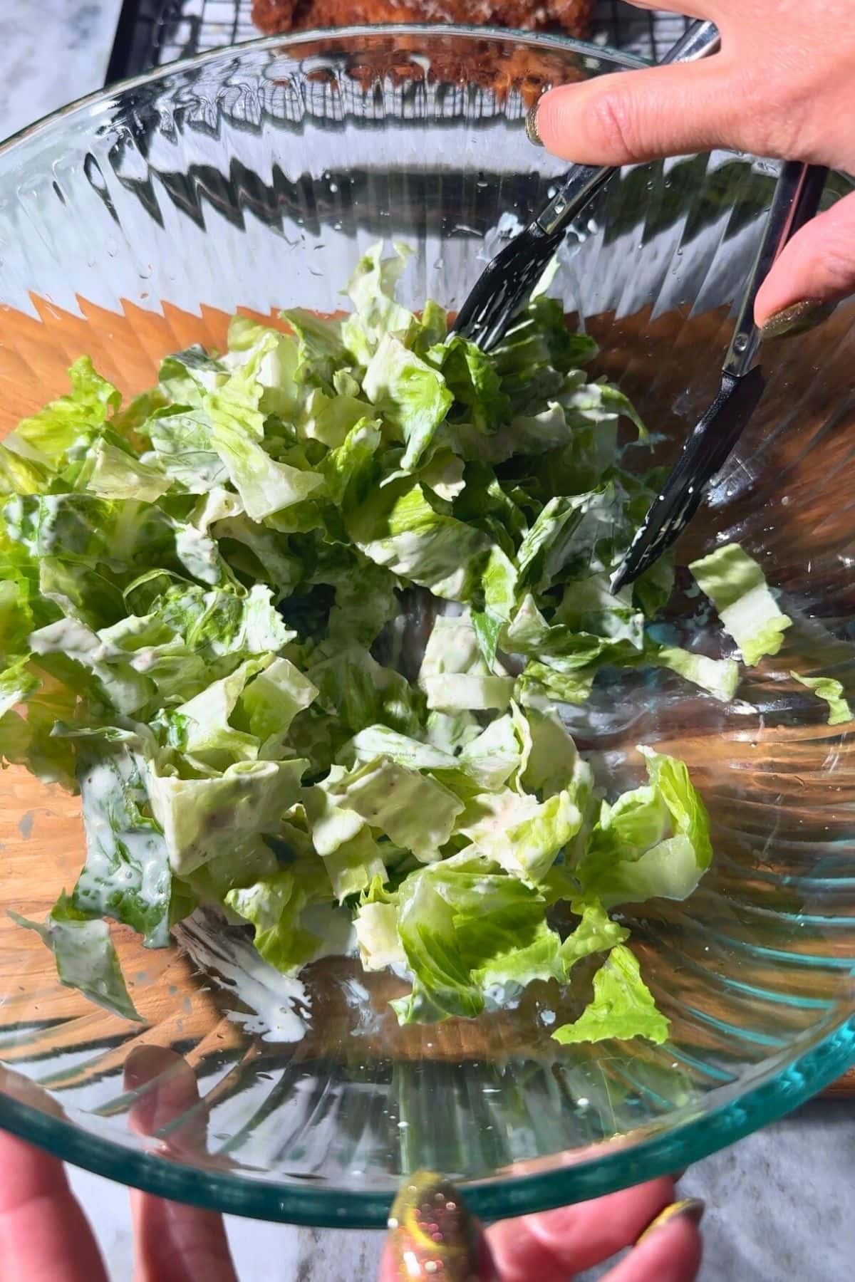 Romain being tossed with homemade Caesar dressing in a mixing bowl.
