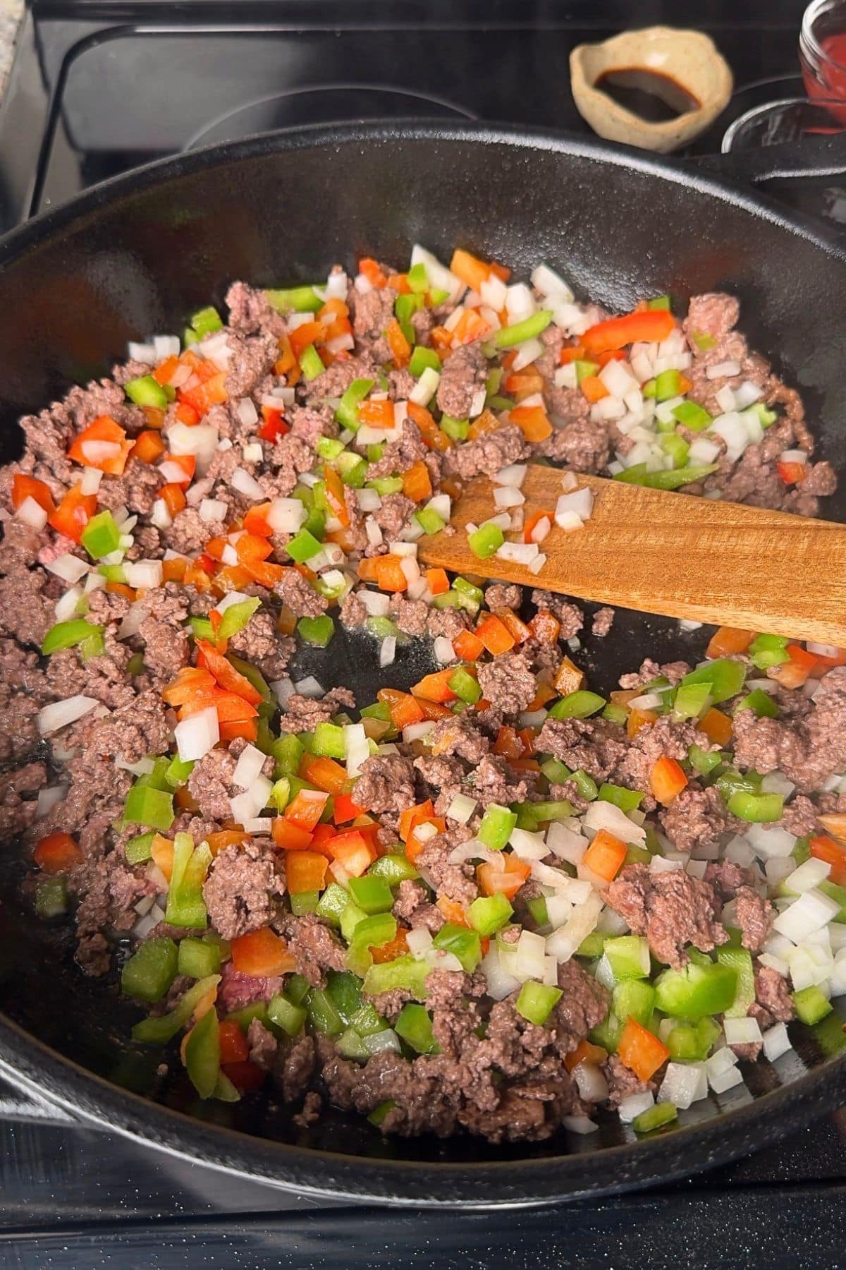 Ground beef and chopped onion, and bell pepper cooking in a pan.
