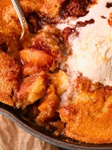 Southern skillet, peach cobbler with a serving spoon to show detail.