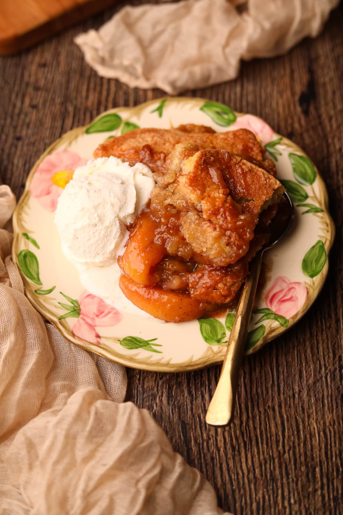 Southern peach cobbler on a dessert plate with a scoop of vanilla ice cream.