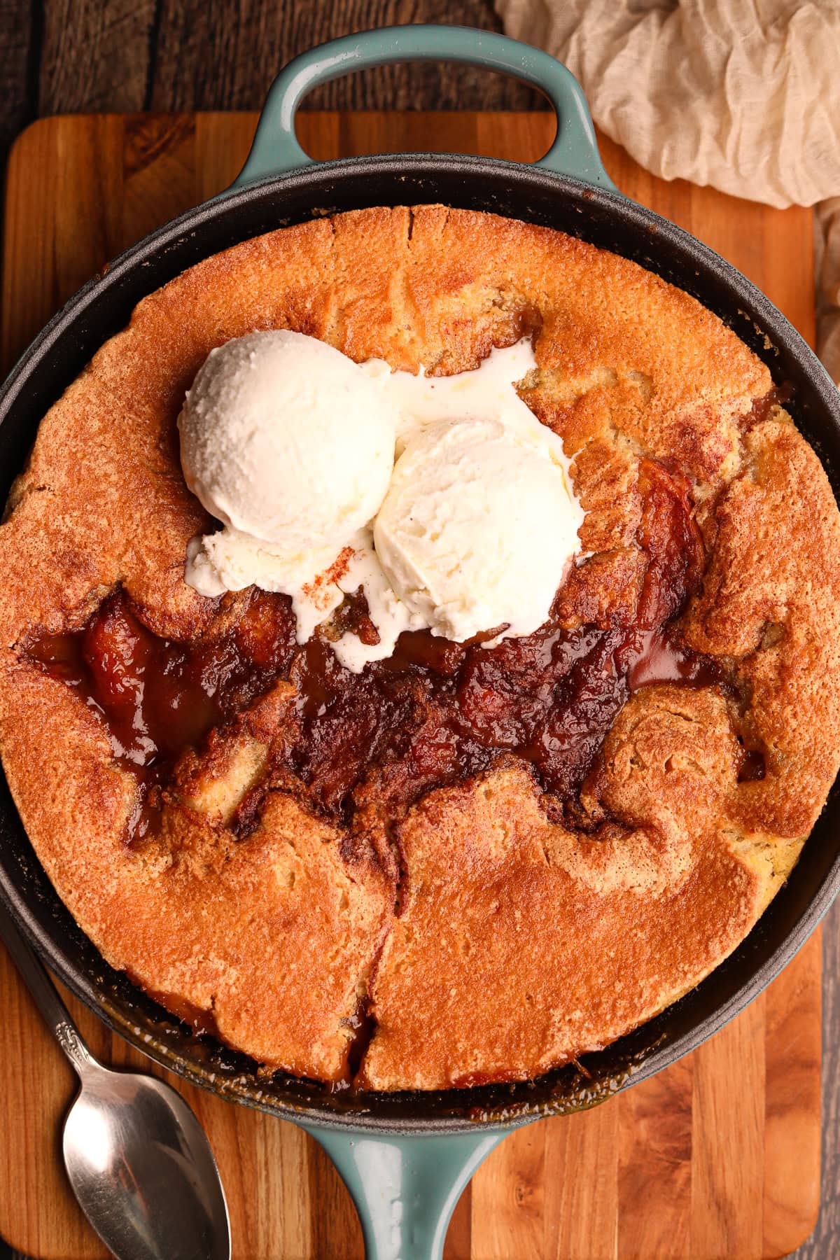 Southern skillet peach cobbler in the pan with two scoops of vanilla ice cream.