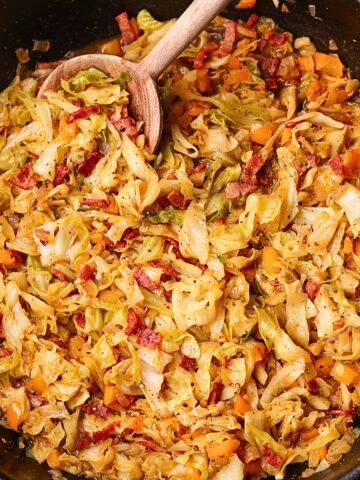 Southern fried cabbage with bacon in a skillet with serving spoon.