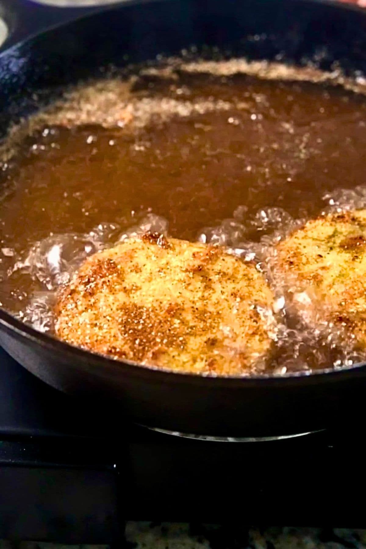 Green tomatoes frying in a cast-iron skillet.