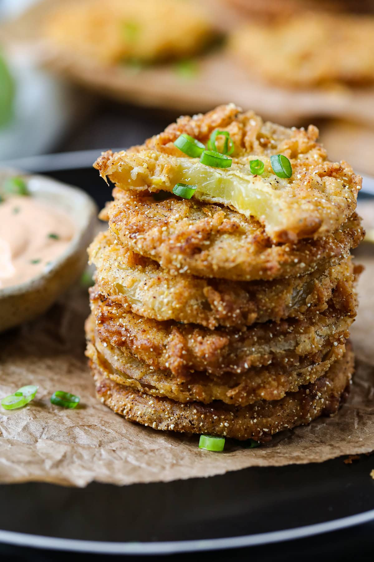 Southern fried green tomatoes stacked on a plate with a bite taken out of the top tomato.